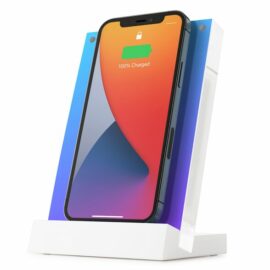 Das Bild zeigt den Twelve South PowerPic Mod Wireless-Charger in Weiß mit einem iPhone, das gerade aufgeladen wird. Das iPhone wird vertikal von dem rahmenähnlichen weißem Ladegerät gehalten, welches das Smartphone zugleich als Bilderrahmen präsentiert. Der Ladezustand des iPhone ist auf dem Display zu sehen und zeigt "100% Charged" an. Das Design des Wireless-Chargers ist minimalistisch und modern, und es ist ersichtlich, dass das Gerät so konzipiert ist, dass es das iPhone stilvoll präsentiert, während es geladen wird.